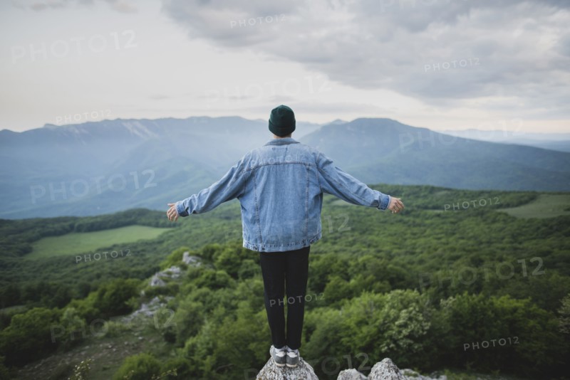 Man standing on cliff by mountain and forest