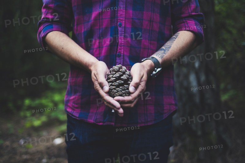 Man wearing checked shirt holding pinecone