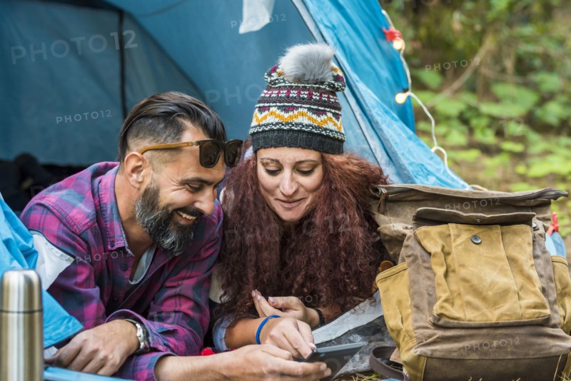 Smiling couple lying in tent using tablet