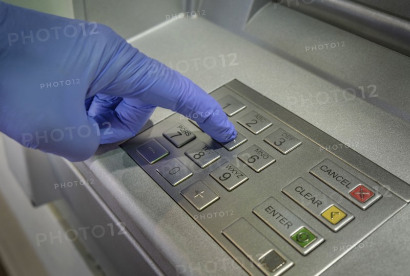 Gloved hand pushing button of cash machine