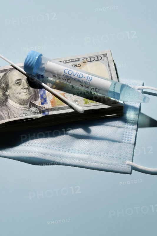 Covid-19 test vial and swab on stack of 100 dollar bills and medical mask