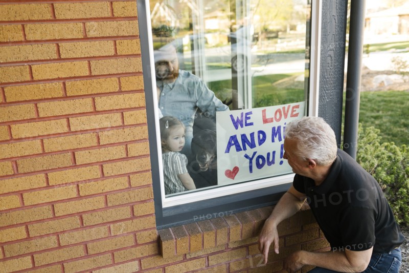 Grandfather visiting family with granddaughter (2-3) through window