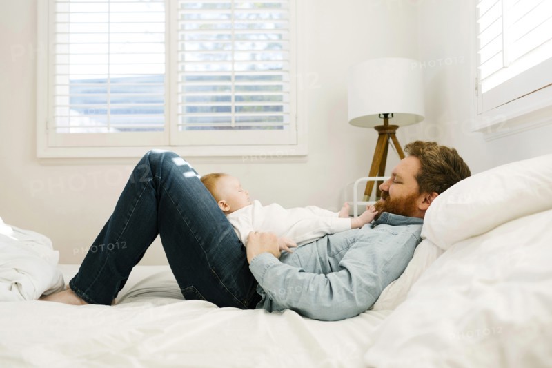 Father lying on bed with baby boy (2-3 months)
