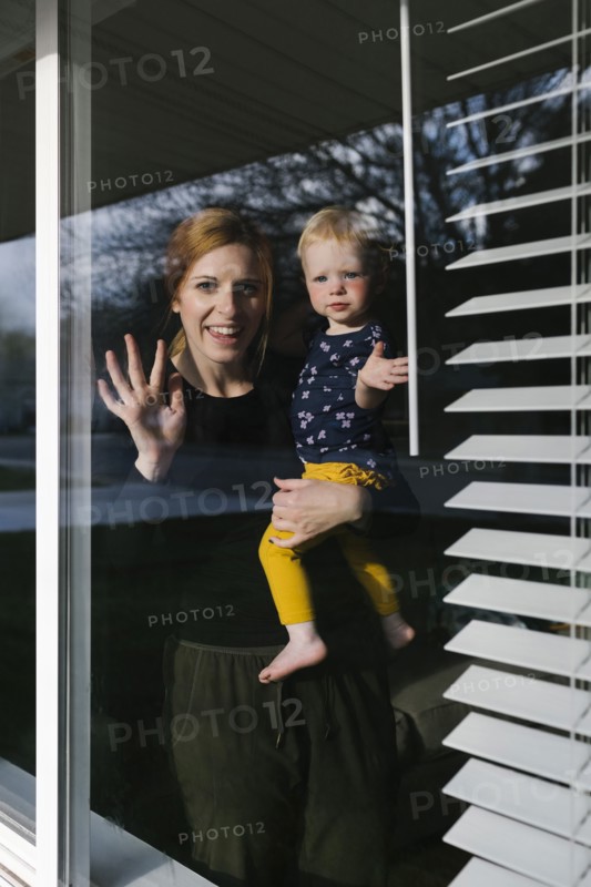 Mother and daughter (2-3) waving through window