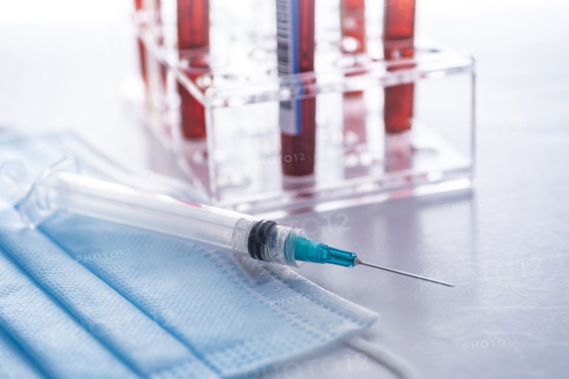 Studio shot of Covid-19 blood samples in test tube rack, syringe and face mask
