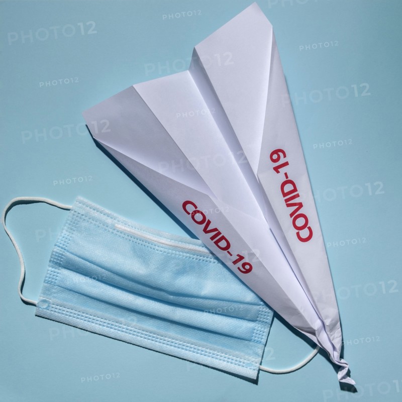 Studio shot of paper plane with Covid-19 sign and surgical mask