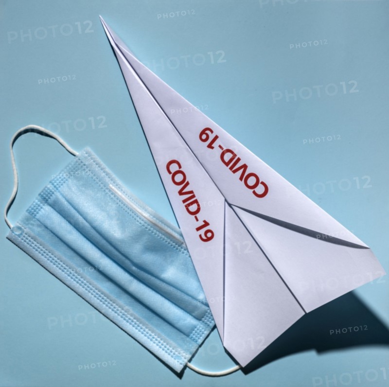 Studio shot of paper plane with Covid-19 sign and surgical mask