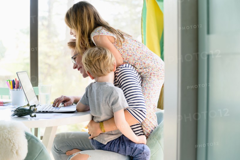 Children (4-5, 6-7) climbing on their mother while she works from home