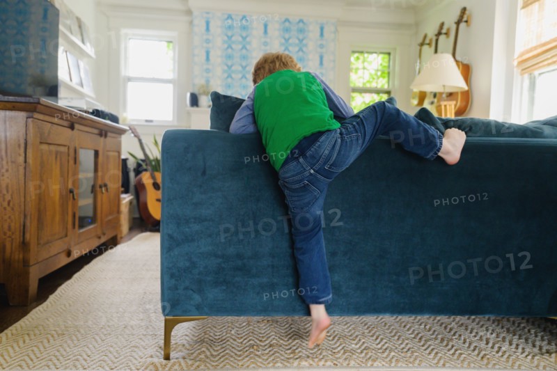 Rear view of boy (4-5) climbing over back of couch
