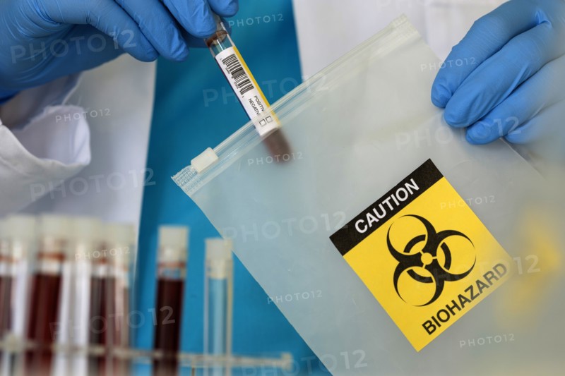 Lab professional putting vial into string bag with biohazard sign