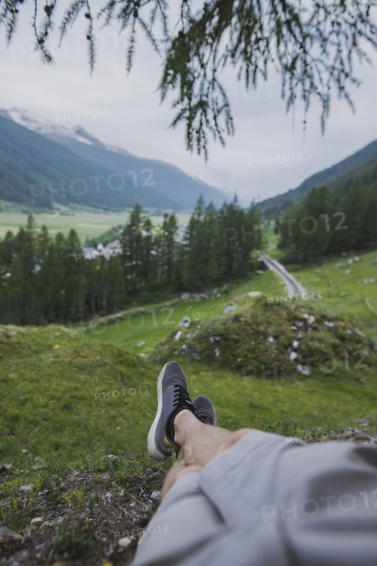 Switzerland, Obergoms, Legs of man relaxing on grass in Swiss Alps