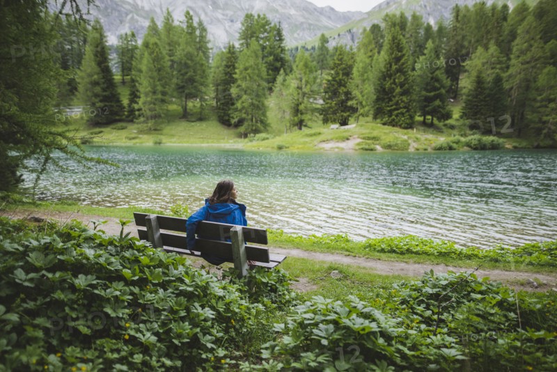 Switzerland, Bravuogn, Palpuognasee, Young woman resting on bench near Palpuognasee lake in Swiss Alps