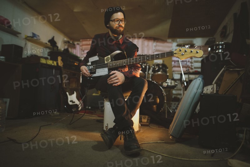Young man playing bass guitar during rehearsal in garage