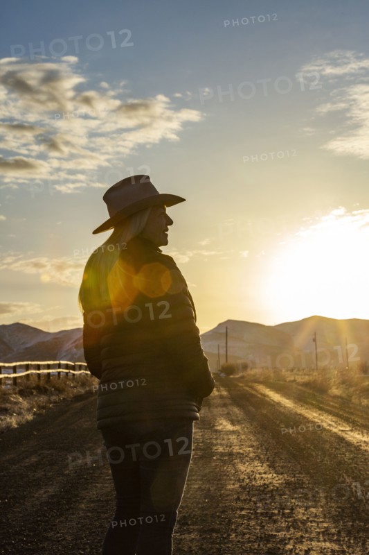 USA, Idaho, Sun Valley, Woman in cowboy hat standing on dirt road at sunset