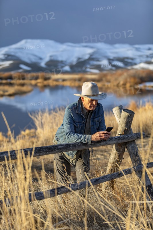 USA, Idaho, Sun Valley, Senior man in cowboy hat leaning against fence