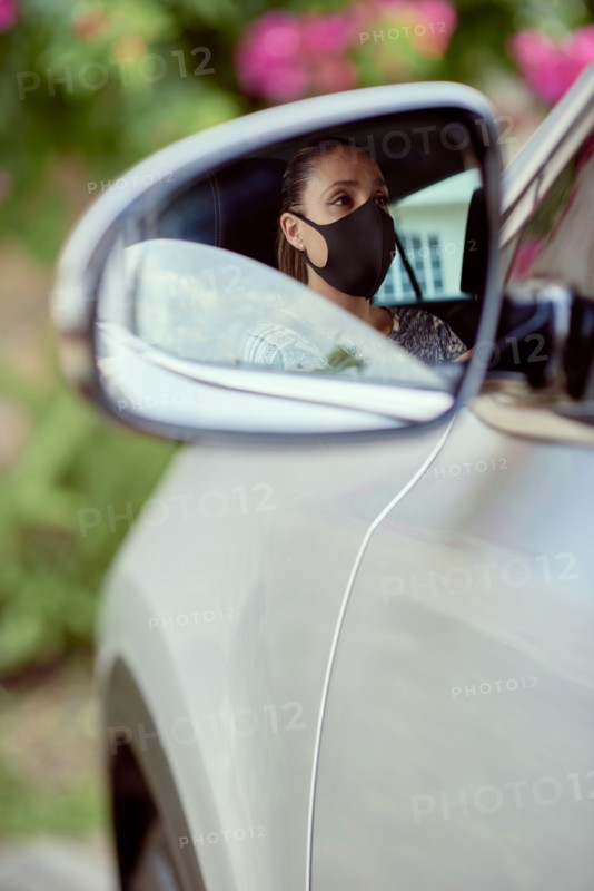 Woman with face mask driving car reflected in mirror