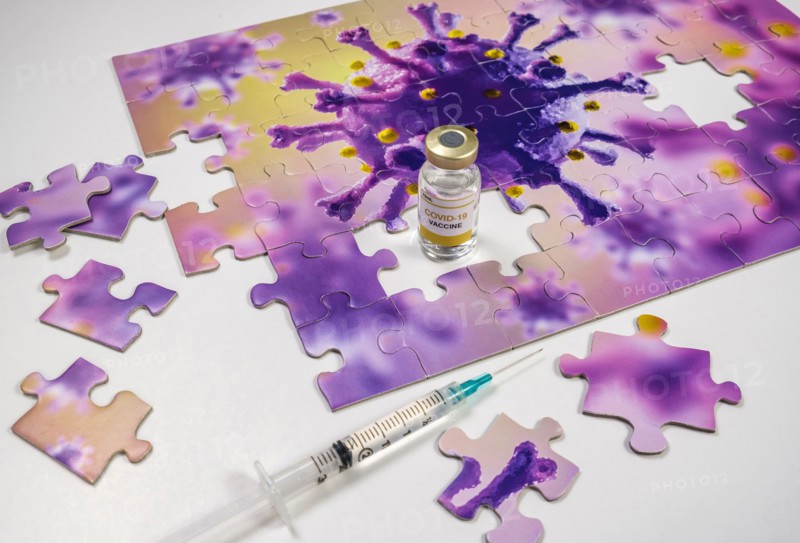 Studio shot of puzzle with Coronavirus model and vaccine vials and syringe