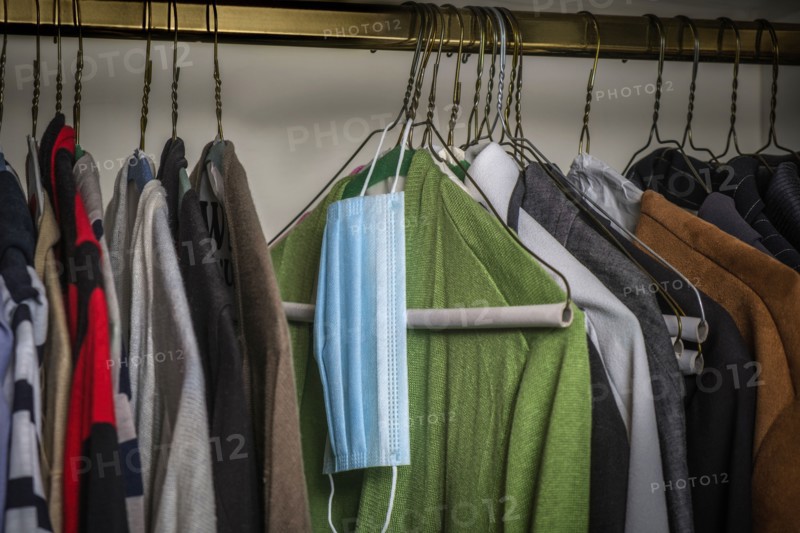 Surgical mask hanging on hanger on rack with clothes