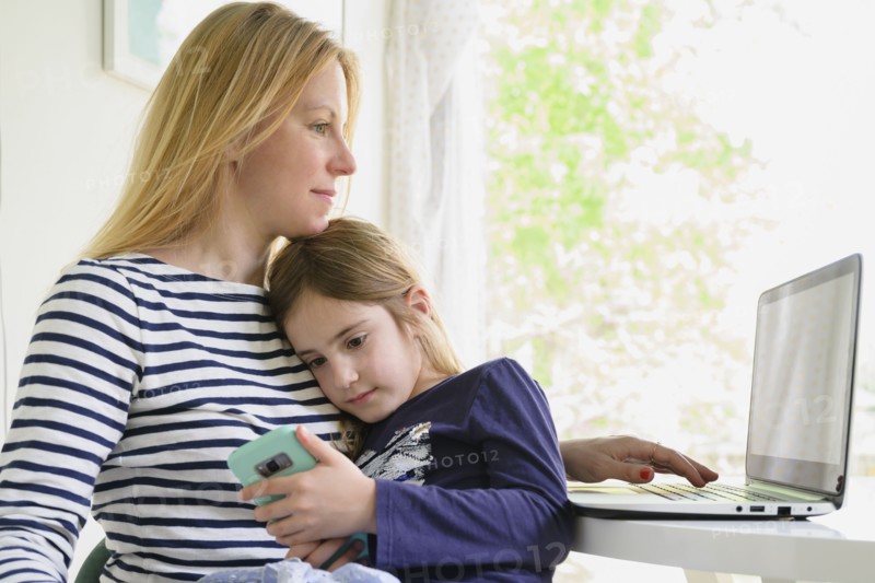 Mother working on laptop while daughter (6-7) using smart phone