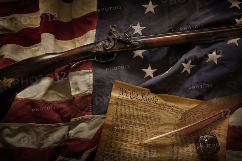 Rifle and US constitution lying on American flag