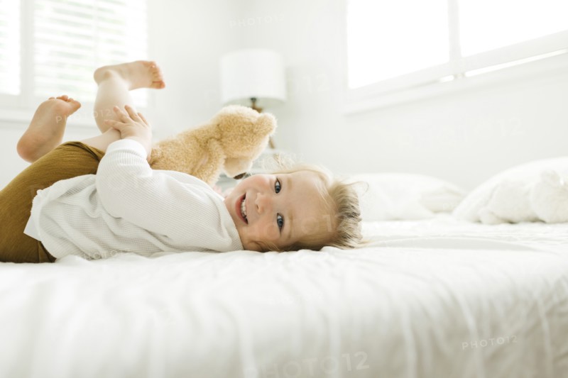 Toddler girl lying on bed with her teddy bear toy