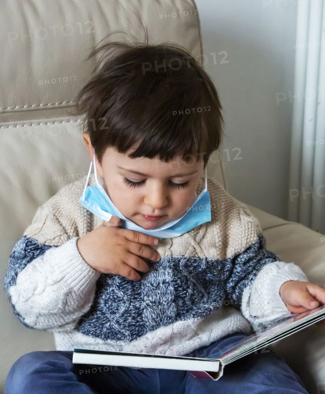 Boy (2-3) wearing face mask holding book