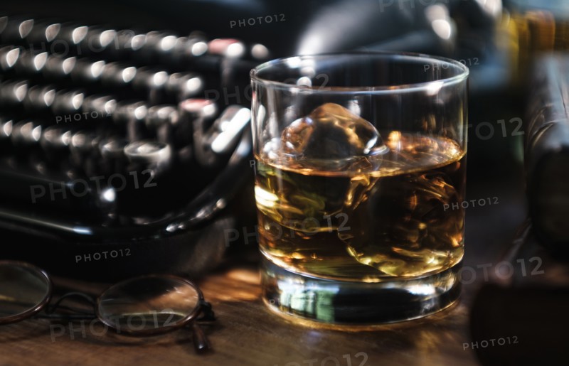 Whiskey glass next to typewriter on desk