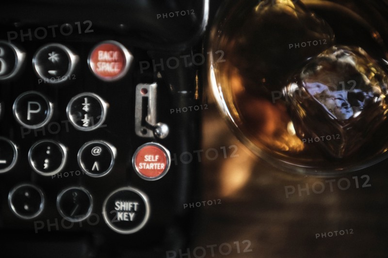 Whiskey glass next to typewriter on desk