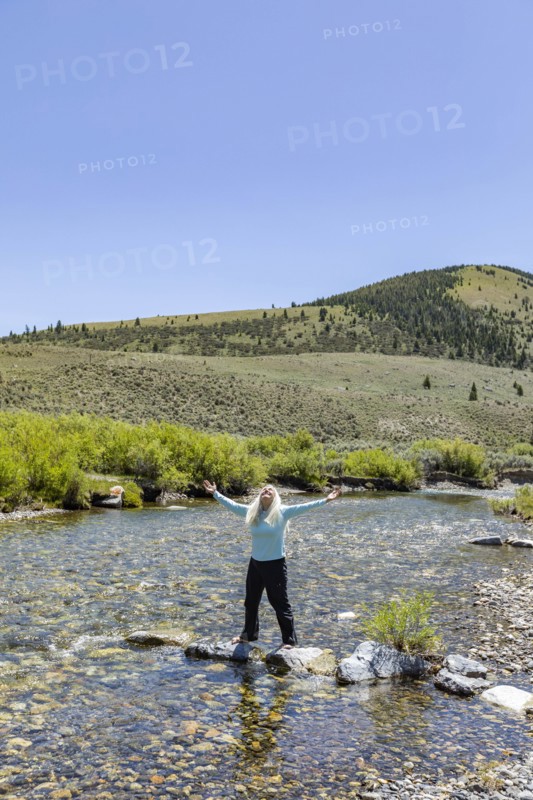 USA, Idaho, Sun Valley, Woman with arms raised standing on rocks in river