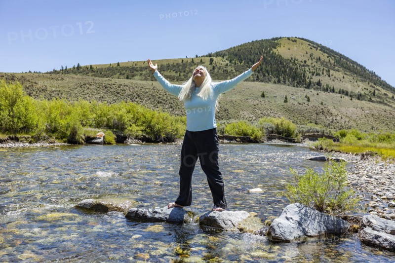 USA, Idaho, Sun Valley, Woman with arms raised standing on rocks in river