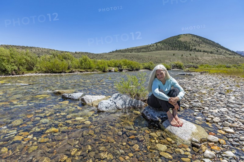 USA, Idaho, Sun Valley, Woman sitting on rock in river