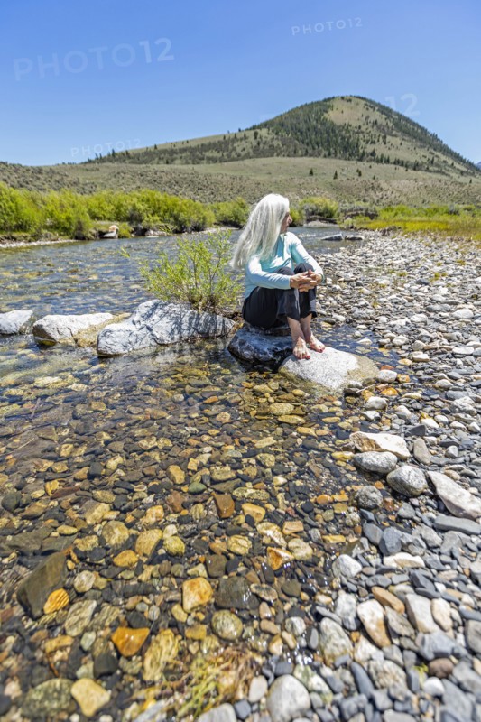 USA, Idaho, Sun Valley, Woman sitting on rock in river