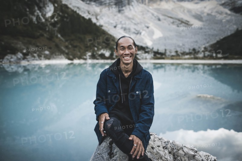 Italy, South Tyrol, Cortina d Ampezzo, lake Sorapis, Portrait of young man sitting on rock at mountain lake