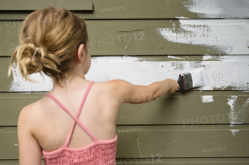 Girl (6-7) painting cottage wall