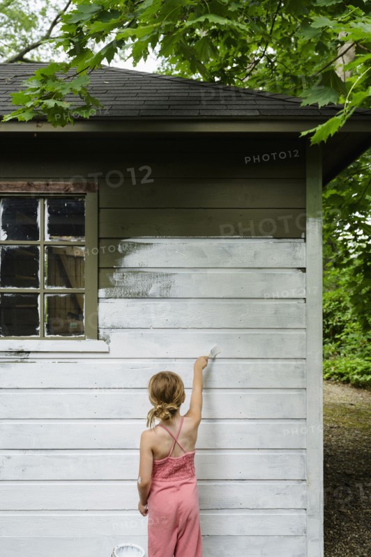Girl (6-7) painting cottage wall