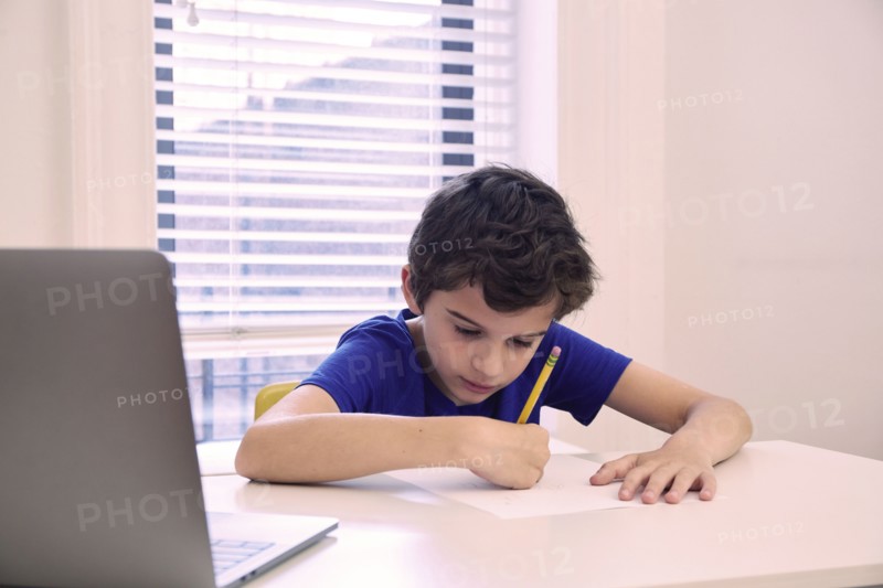 Boy (8-9) writing test at during remote lesson at home