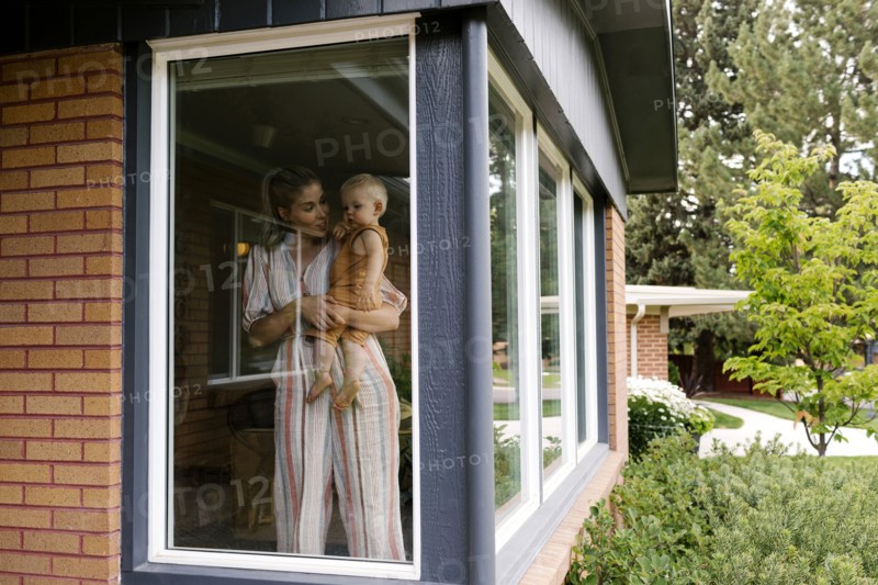 Mother with baby son (18-23 months) standing behind window
