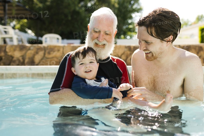 Grandfather, son and grandson (2-3) standing in outdoors swimming pool
