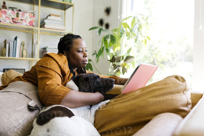 Woman reading book on sofa with her dog