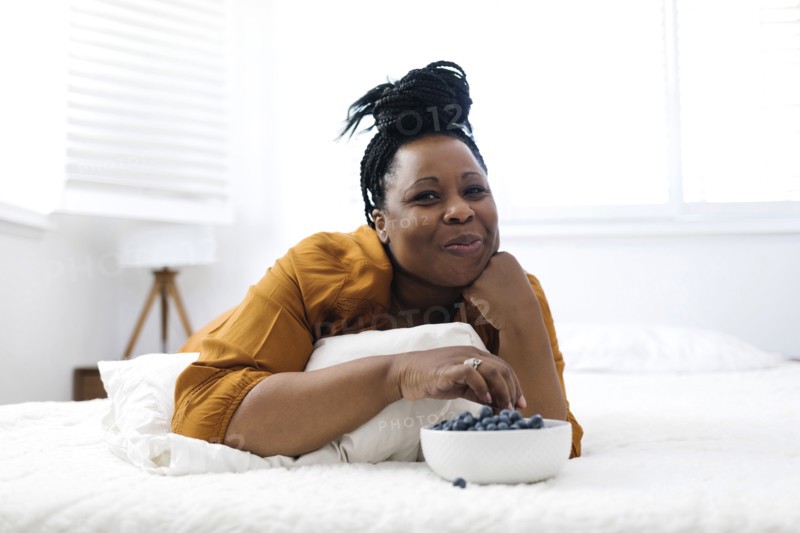 Woman lying on bed, eating blueberries and watching tv