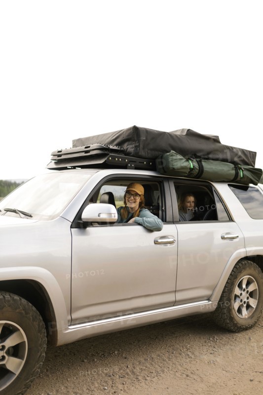 Smiling woman with daughter (6-7) sitting in off road car with tent on roof
