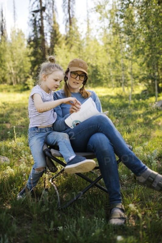 USA, Utah, Uinta National Park, Mother and daughter (6-7) doing crossword in meadow in forest