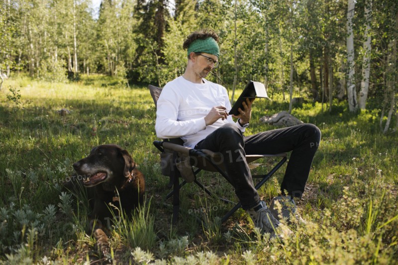 USA, Utah, Uinta National Park, Man with dog sitting in meadow in forest, using tablet
