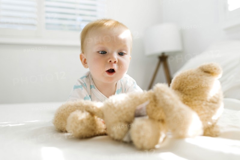 Baby boy (6-11 months) looking at teddy bear on bed