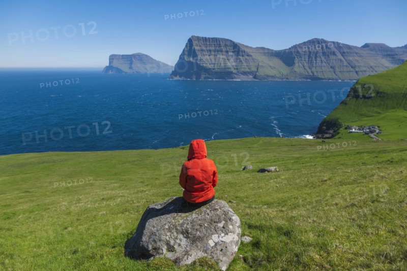 Denmark, Faroe Islands, Klaksvik, Trollanes, Woman sitting on rock and looking at ocean