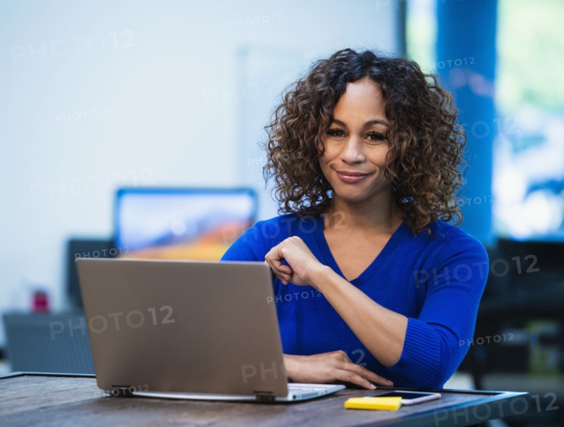 Portrait of smiling woman sitting at desk with laptop in office