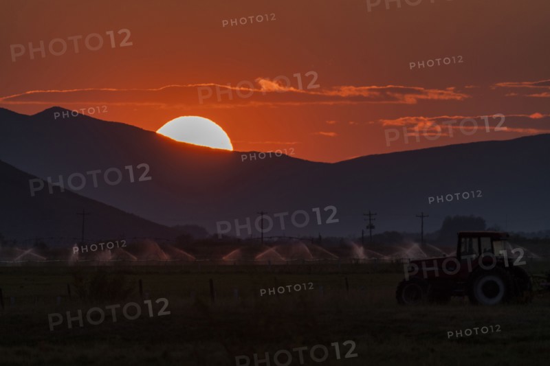 Irrigation equipment in field and sun setting behind mountain