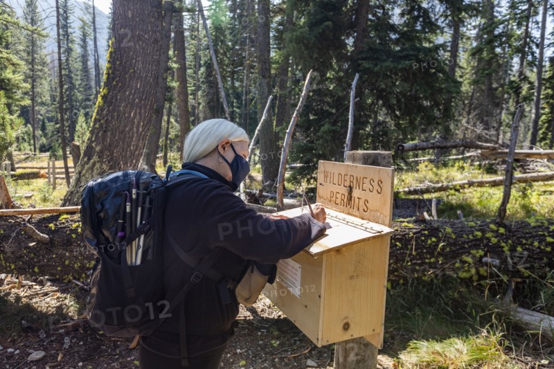 Senior woman in protective mask signing wilderness permit before hiking
