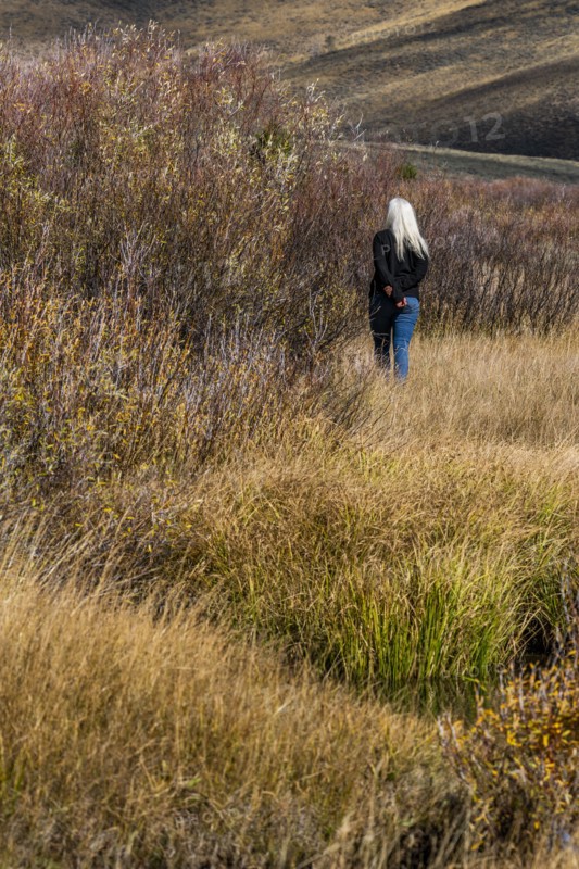 Senior woman with long white hair walking by stream among grass in non urban landscape