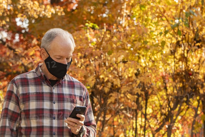 Senior man wearing Covid protective mask using smartphone outdoors in fall